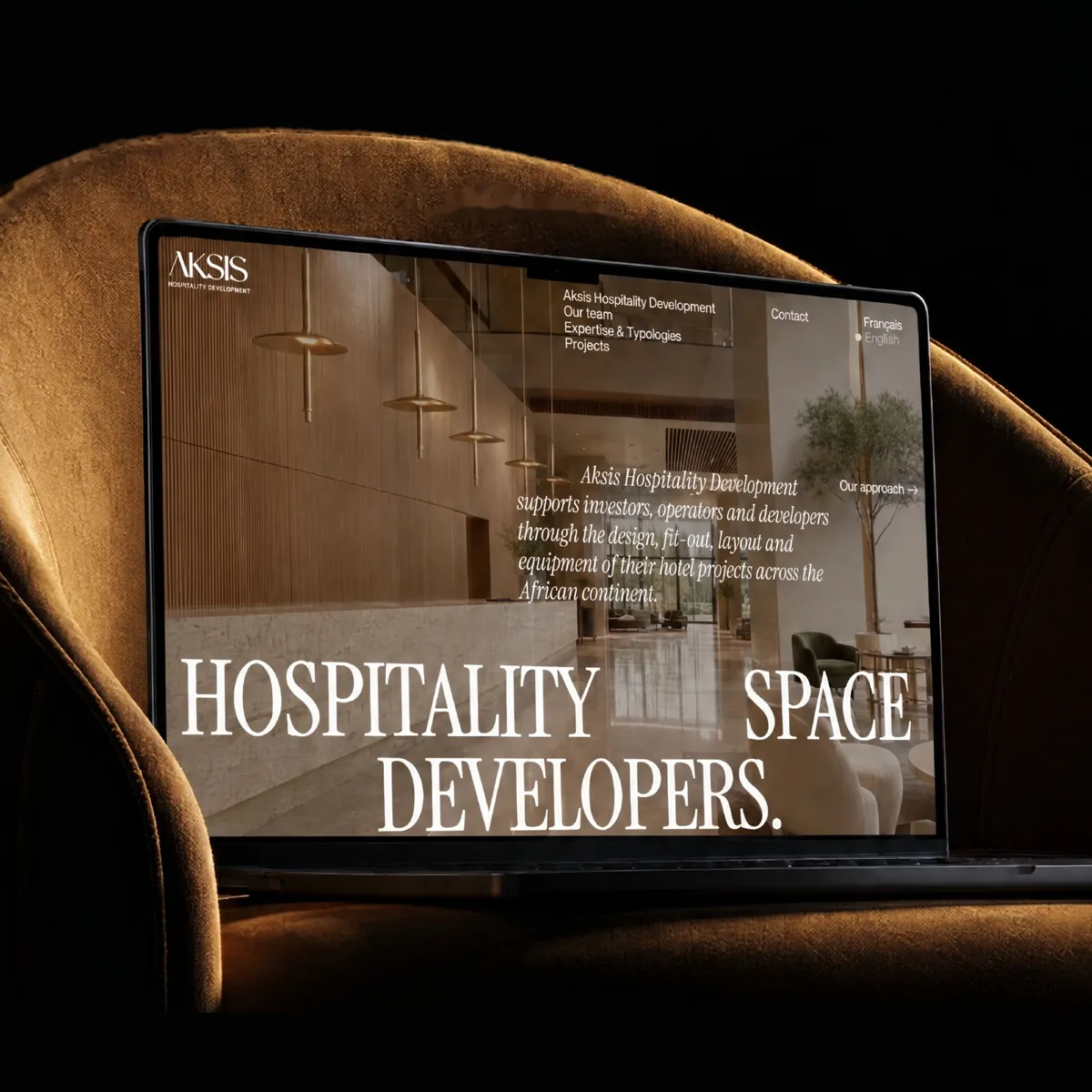 Aksis Hospitality Development homepage open on a MacBook, full bleed hotel lobby photography behind the display serif headline
